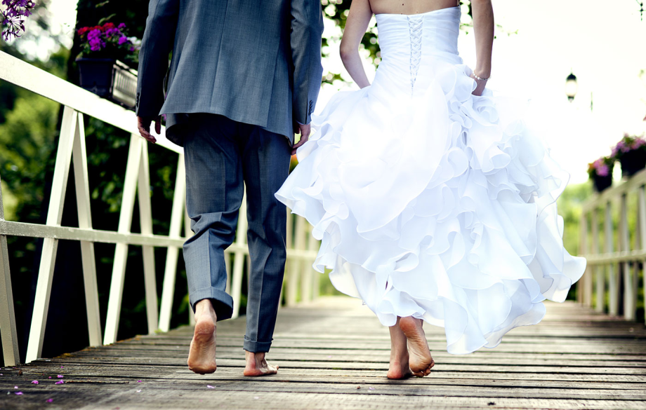 A bride and groom walking barefoot across a wooden footbridge